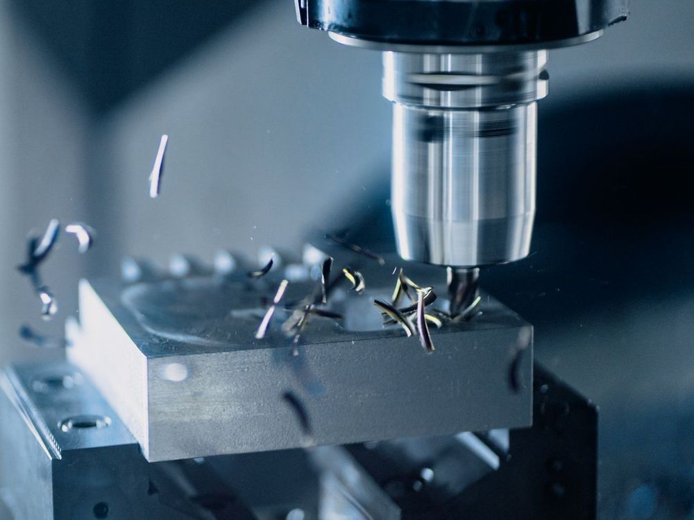 Close-up of a CNC milling spindle cutting an aluminum block held in a vise, with chips flying